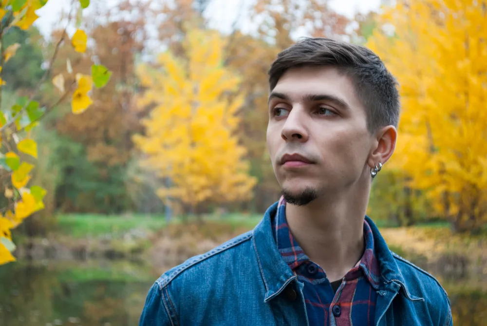 Young man outside during the autumn season wears a denim jacket and short hair with an example of chin patch goatee styles