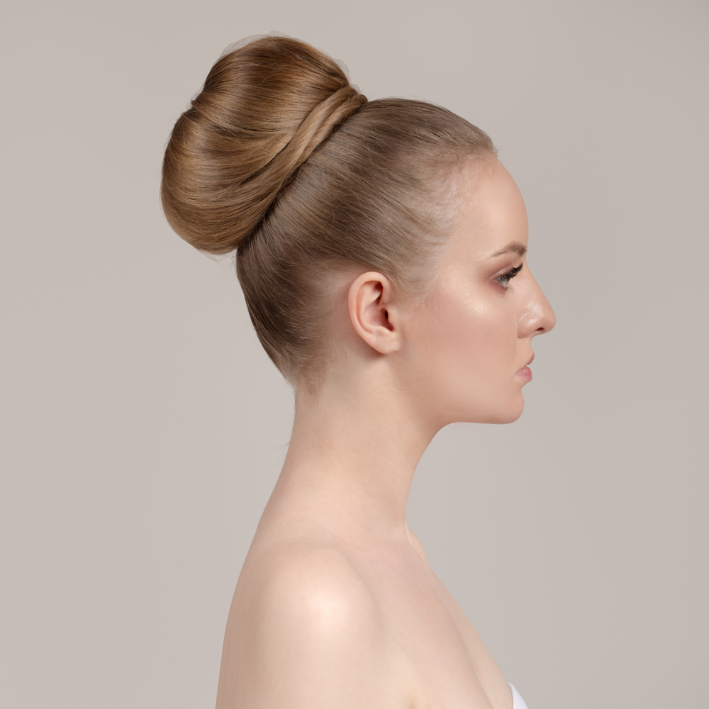 Side view of woman with bare shoulders rocking a jumbo sleek ballerina bun to show what hair loss hairstyles for thinning hair on crown look like