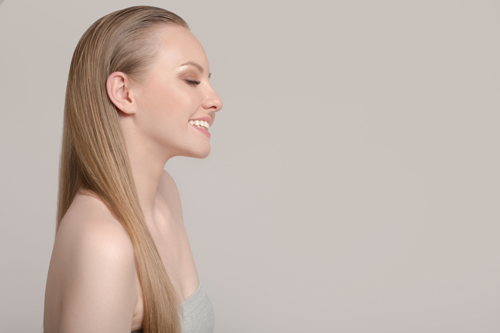 Side view of smiling woman with her eyes closed with her long hair slicked back as an example of hairstyles for thinning hair at the crown