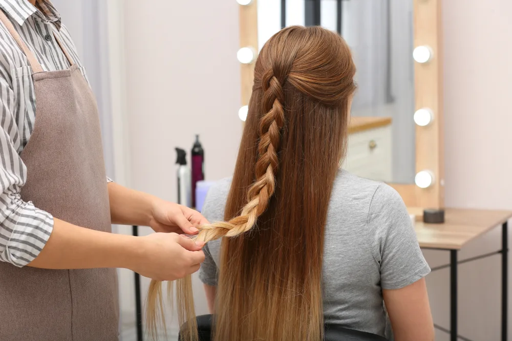 Half up braid hairstyle for long straight hair shown as stylist does a client's hair in the salon
