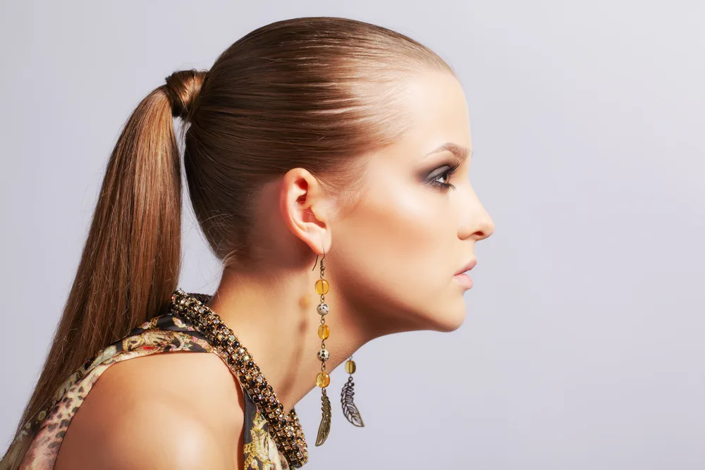 Side view of a woman looking serious to show her wrapped ponytail with sleek texture in front of a gray background