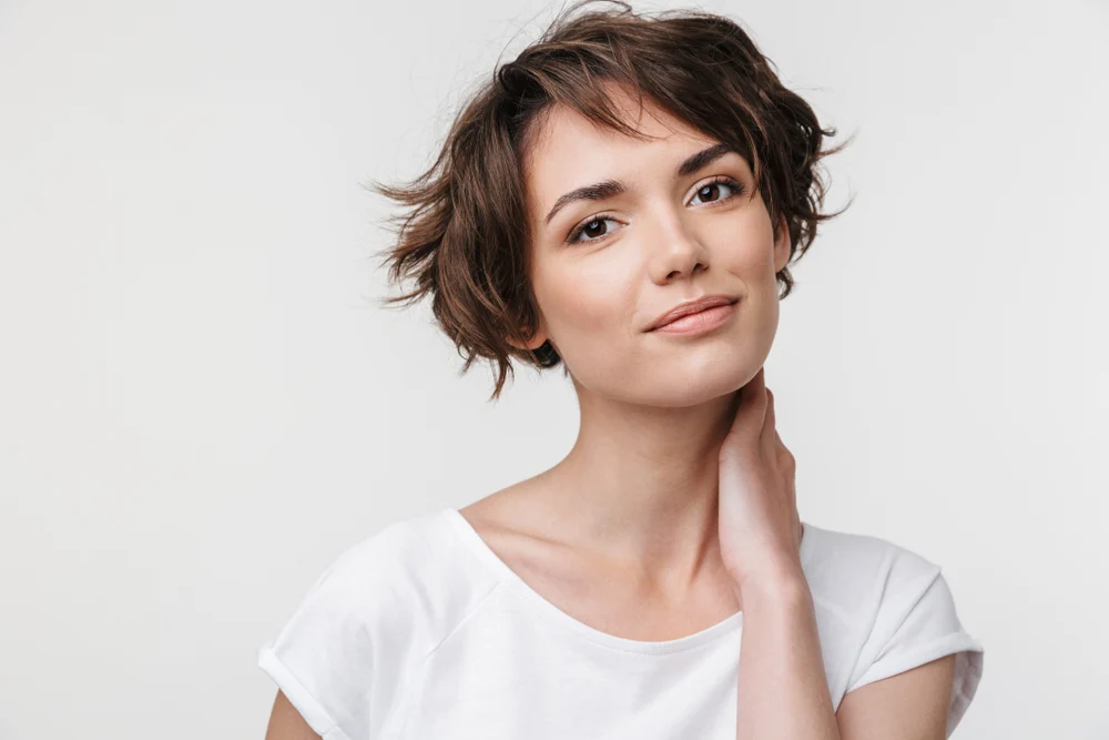 Young woman holds her neck while wearing a white t-shirt and messy bob hairstyle with layers that suit fine or thin hair