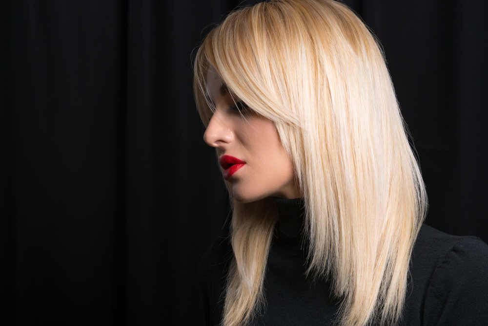 Woman in black outfit shows off blonde hair with graduated layers and curtain bangs as one of the top low maintenance haircuts for women in front of a black background
