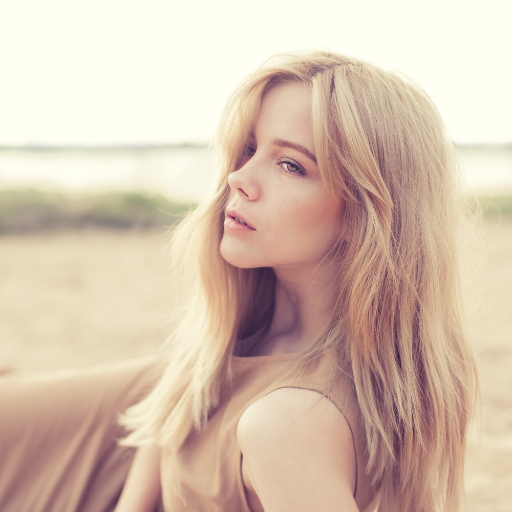 Woman lies on the beach looking away with her long blonde hair styled with bangs and layers to show one of the best low maintenance haircuts for women