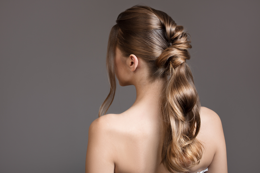 Back view of a brunette woman with bare shoulders and a chic curled and twisted ponytail style 