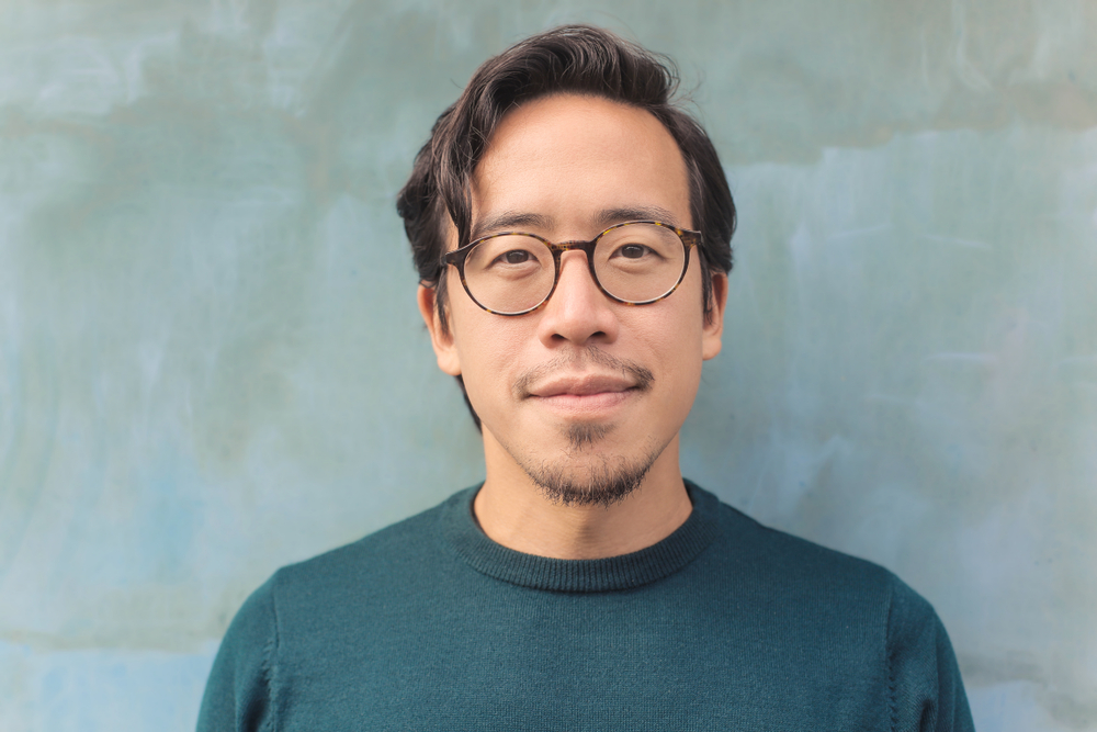 Asian man with glasses wears a teal shirt and shows off a tapered cut with bangs, which is one of the best low maintenance haircuts for men