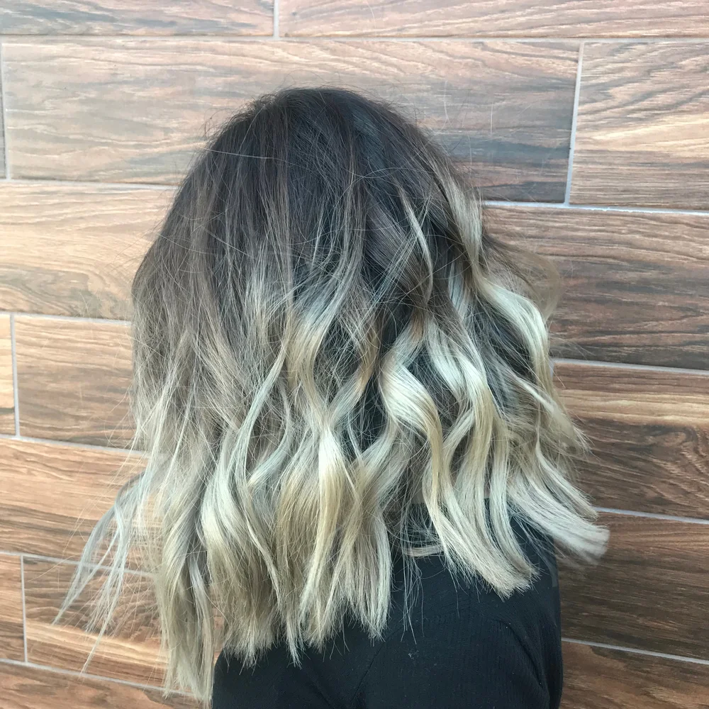 Side of woman's balayage hairstyle with waves and medium length shown on her thick hair in front of a wood plank wall