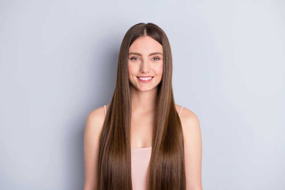 Portrait of a brunette woman smiling and showing off one of the easiest hairstyles for long straight hair, leaving it down and loose with a middle part