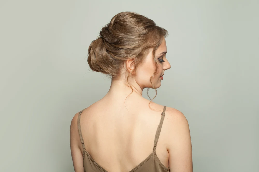 Back profile view of young brunette woman wearing an upswept updo, an example of trendy homecoming hairstyles in style right now