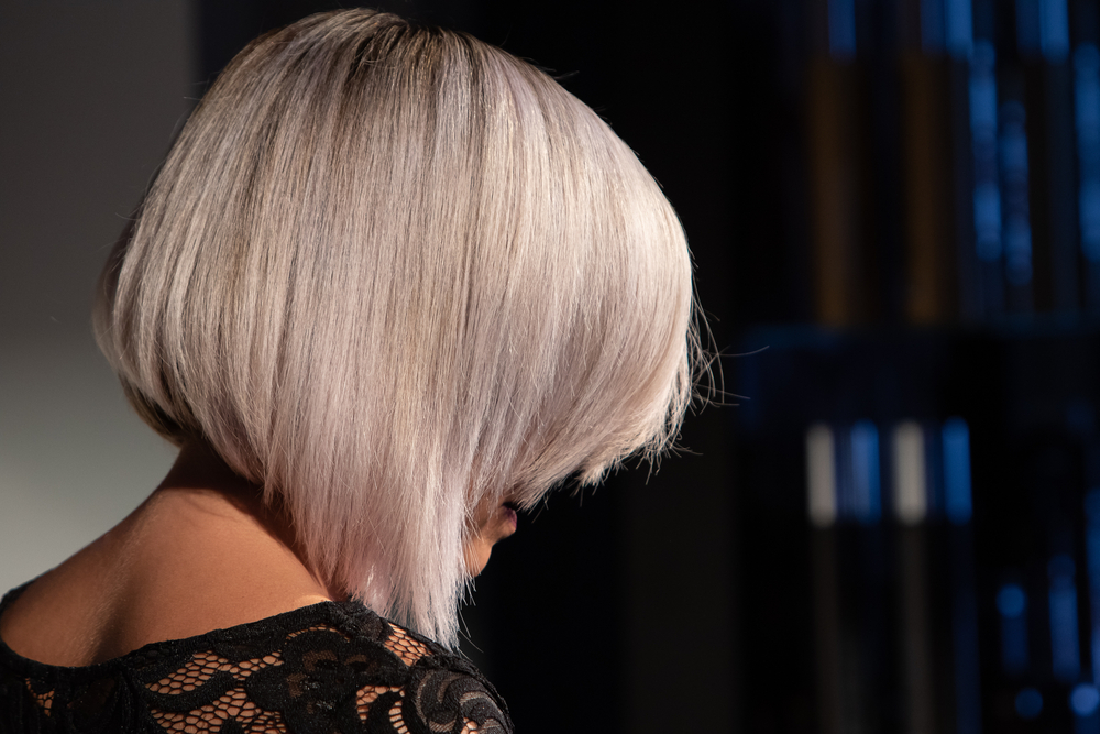 Back side view of platinum blonde woman's head featuring one of the most popular low maintenance medium length hairstyles for thick hair with an a-line bob