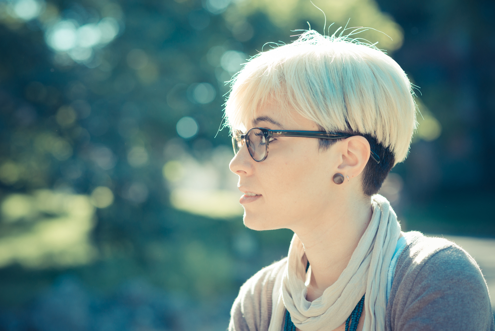 Side view of a woman wearing glasses and a short pixie haircut for fine thin hair with underdyed color sits outside