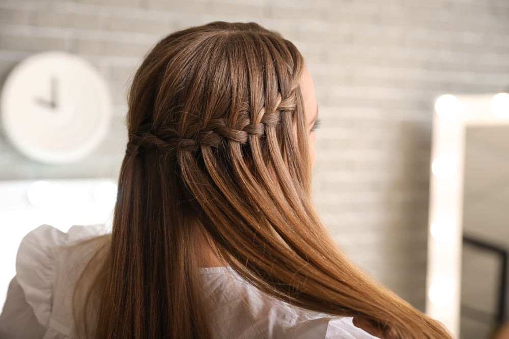 Back profile view of woman with one of the best hairstyles for long straight hair featuring a half up waterfall braid