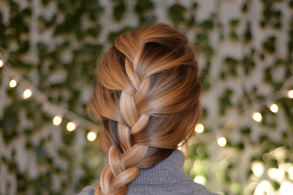 Rear view of woman with highlighted hair in a room with ivy and string lights wearing a French braid, which is one of the best hair loss hairstyles for thinning hair on crown