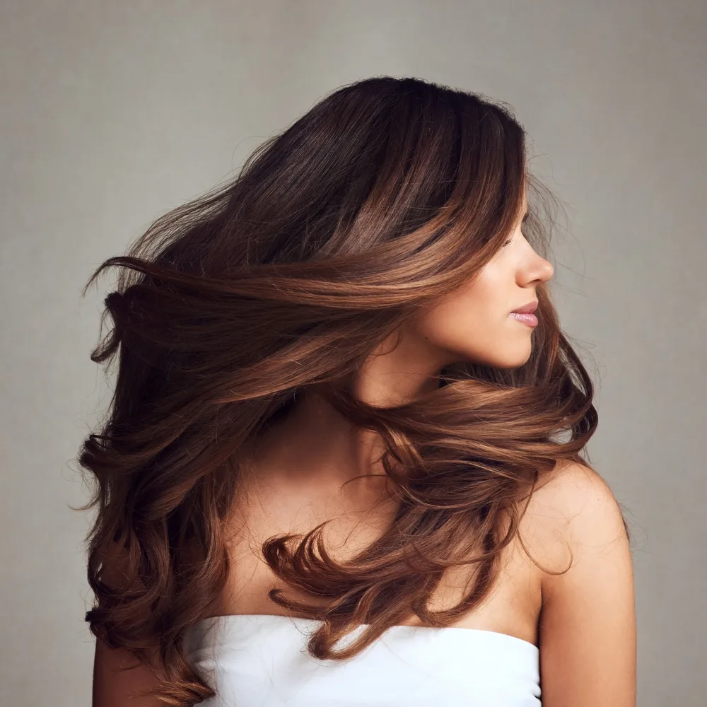 Side view of brunette woman with long hair styled in a blowout, an example of great hairstyles for long straight hair