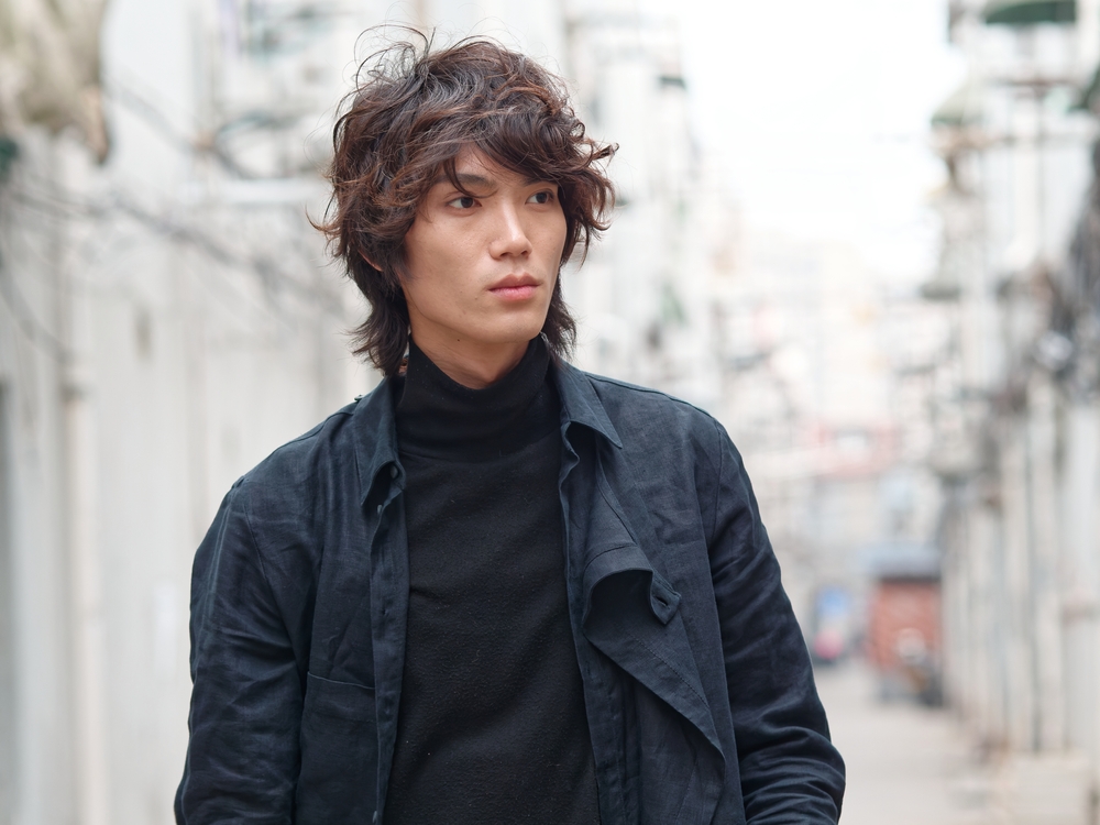 Asian man poses on the street with a serious expression and black jacket as he rocks a long shag, one of the best low maintenance haircuts for men