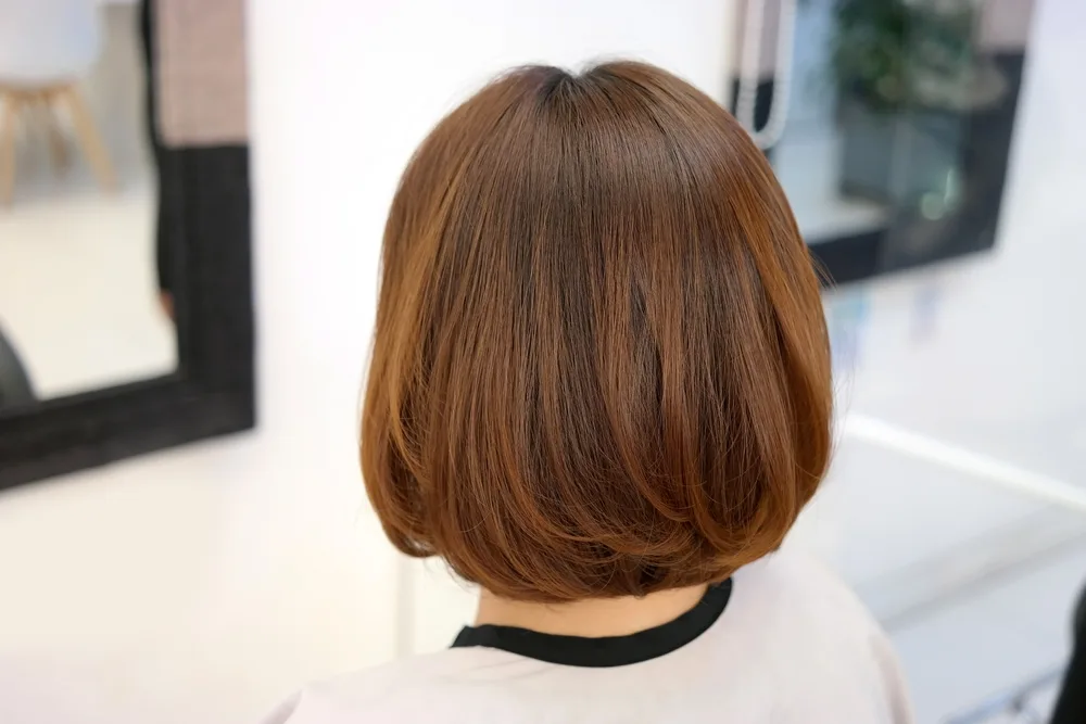 Rear view of light brown hair cut in a low maintenance medium length hairstyle for thick hair with layers at the ends