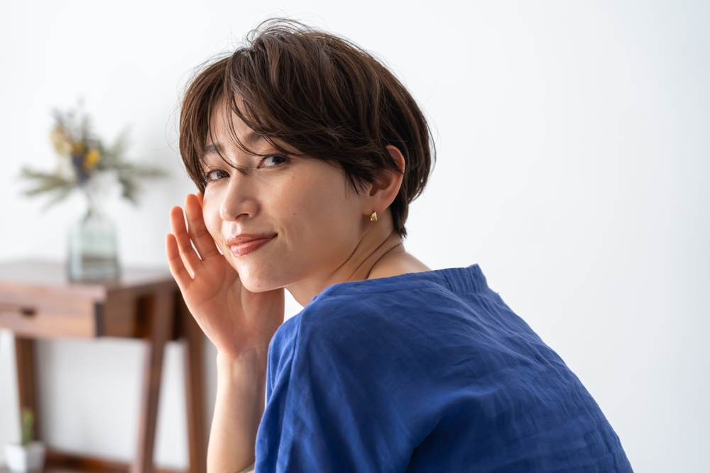 Young Asian woman in a blue shirt looks back over her shoulder with a layered long pixie cut, one example of fine hair thin hair low maintenance hairstyles highlighted in this guide