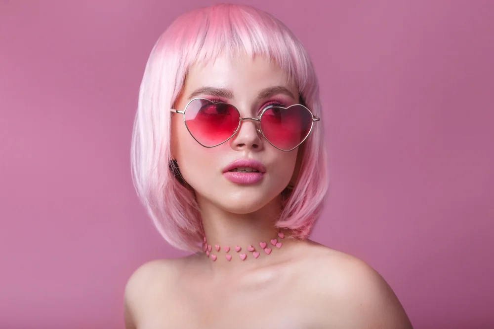 Close-up of woman with bare shoulders wearing pink round sunglasses and a pink bob hairstyle for fine thin hair as an example of low maintenance short hairstyles that make hair look fuller