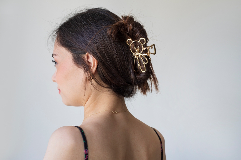 Back side view of brunette woman wearing a teddy bear claw clip updo hairstyle in front of a gray wall