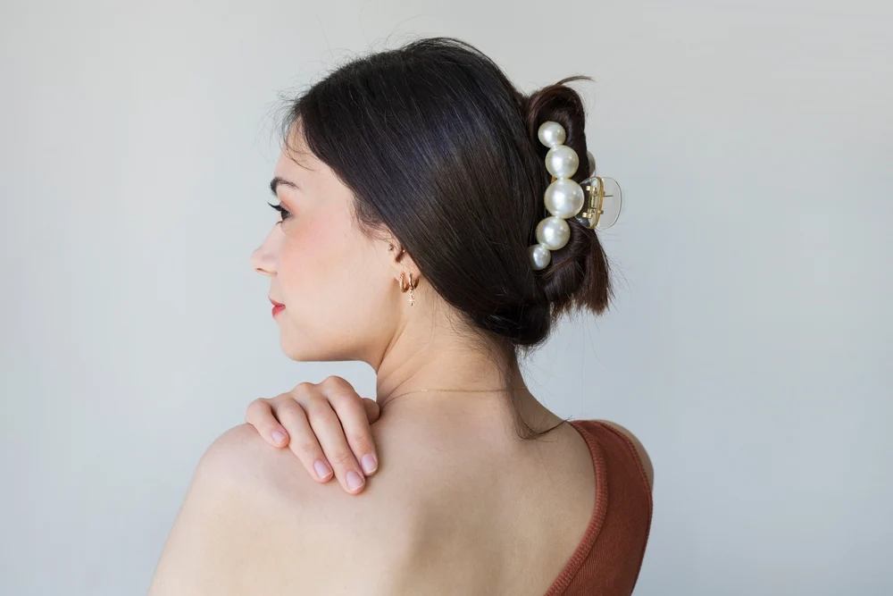Back view of woman with hand on her shoulder turned to the side wearing one of the best hair loss hairstyles for thinning hair on crown, a claw clip updo