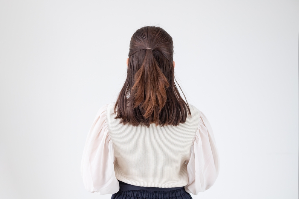Back view of a brunette woman in a white top with puffy sleeves wearing a simple half-up hairstyle to cover thinning hair on the crown