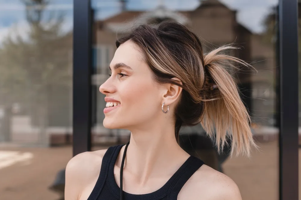 Smiling woman in a black tank top looks to the side to show off her claw clip fountain ponytail with sporty vibes