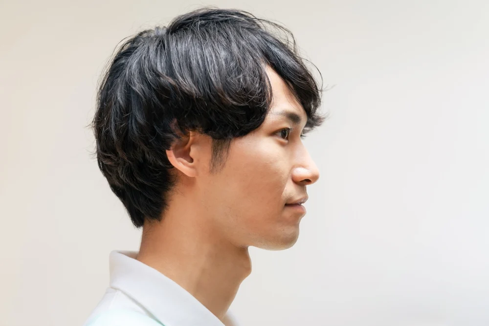 Asian man's side profile view shows the layers in his medium length low maintenance haircut while he wears a white collared shirt