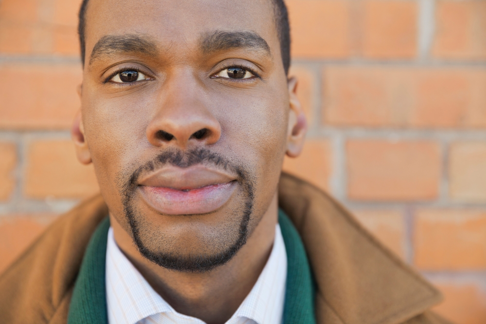 African American man wearing a coat in front of a brick wall models a circle beard goatee with no soul patch
