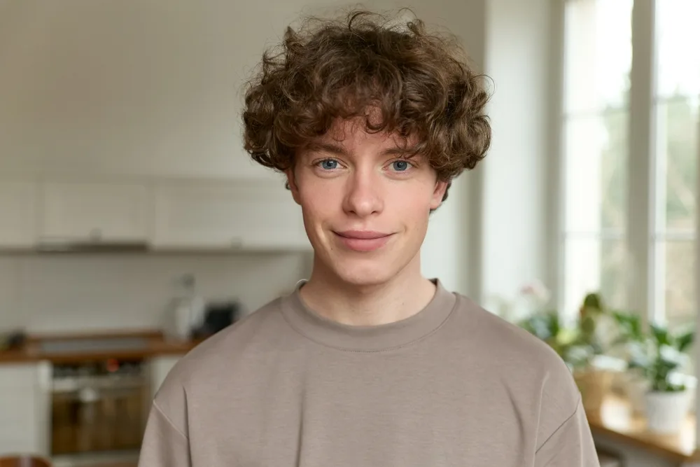 Man with messy curly hair in a tan t-shirt looks at the camera as an example of low maintenance haircuts for men
