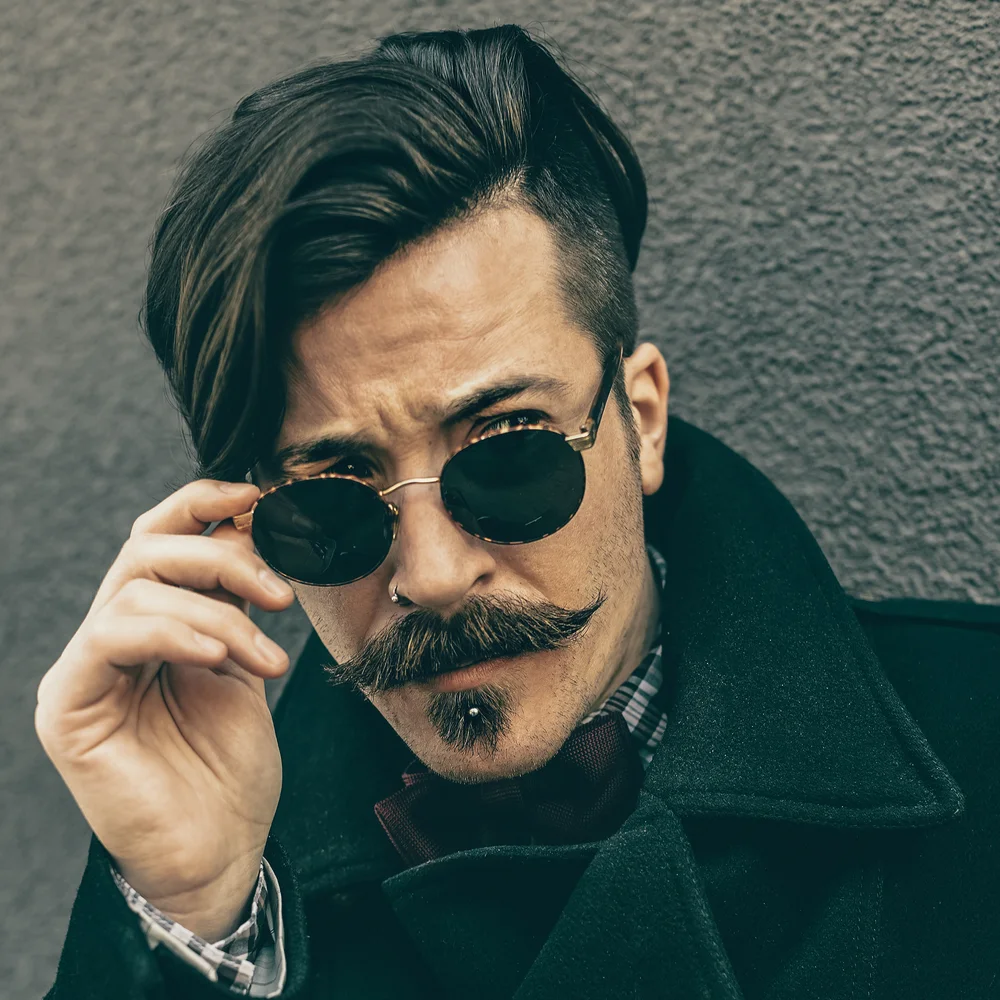 Stylish man with long hair and rounded sunglasses with a lip piercing wears an English mustache, one of the historic mustache styles for men