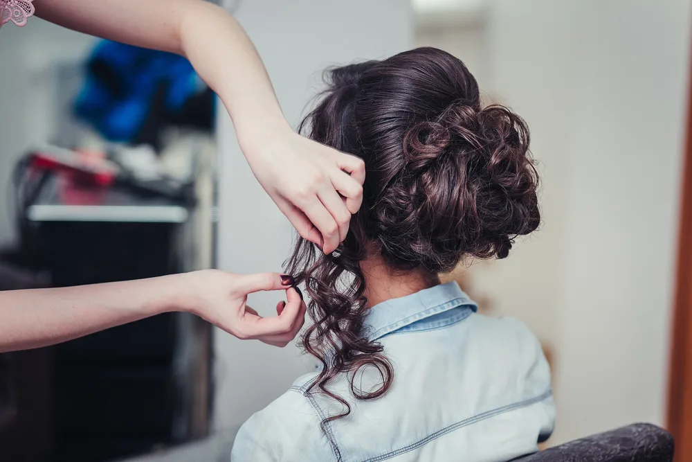 Back side view of stylist doing a brunette woman's homecoming hairstyles with a curly updo