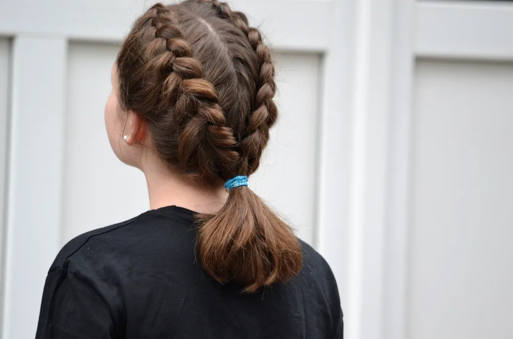 Back view of brunette woman looking up with double dutch braids as an example of elevating ponytail hairstyles