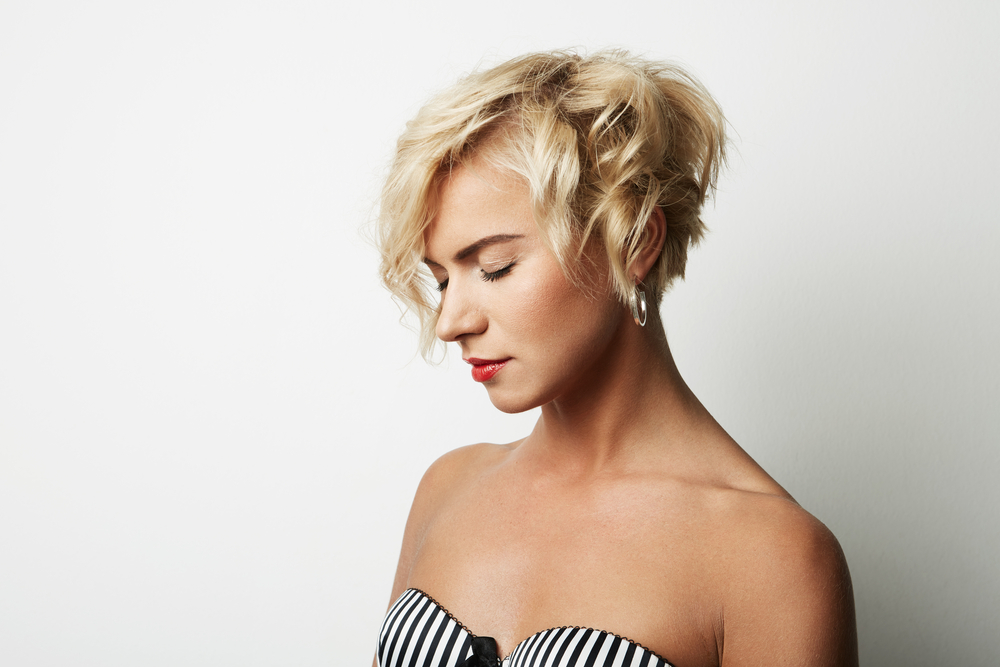Blonde woman looks down with closed eyes wearing a striped top and messy pixie cut with curls 