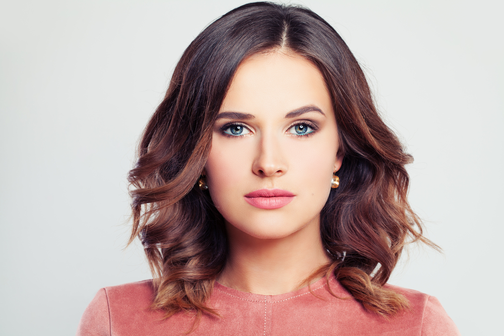 Serious brunette woman wears a medium length hairstyle for thick hair with face-framing layers and waves