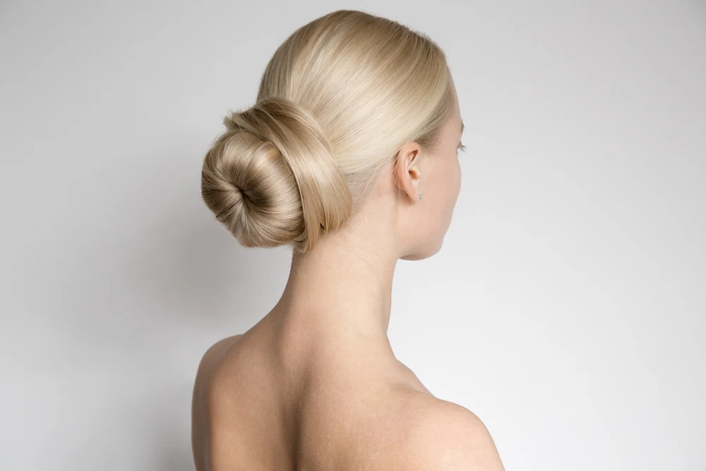 Woman with bare shoulders wears a donut bun with the ends wrapped and pinned for a list of hairstyles for long straight hair