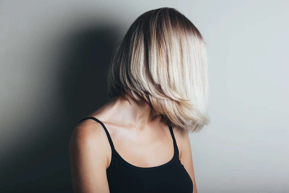 Blonde woman with hidden face looks to the side to show one of the best low maintenance haircuts for women, a lob with short layers