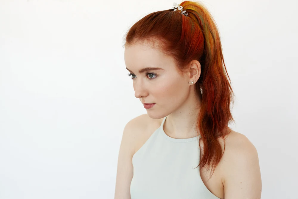 Woman with red hair in a white halter top looks away and models a high ponytail secured with a spiral hair tie