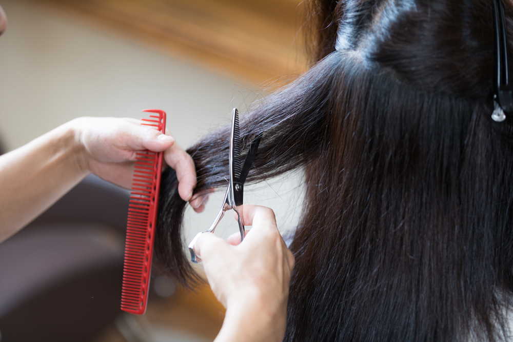 Hairdresser holds out a section of thick brown hair to use thinning shears to remove some bulk and weight for a low maintenance medium length hairstyle for thick hair