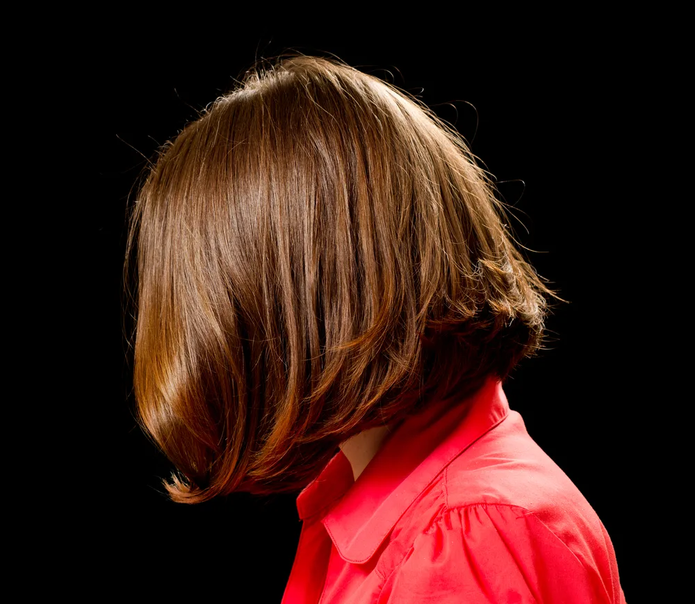 Side view of woman's head with one of the best low maintenance medium length hairstyles for thick hair featuring short layers as she wears a red shirt in a dark room